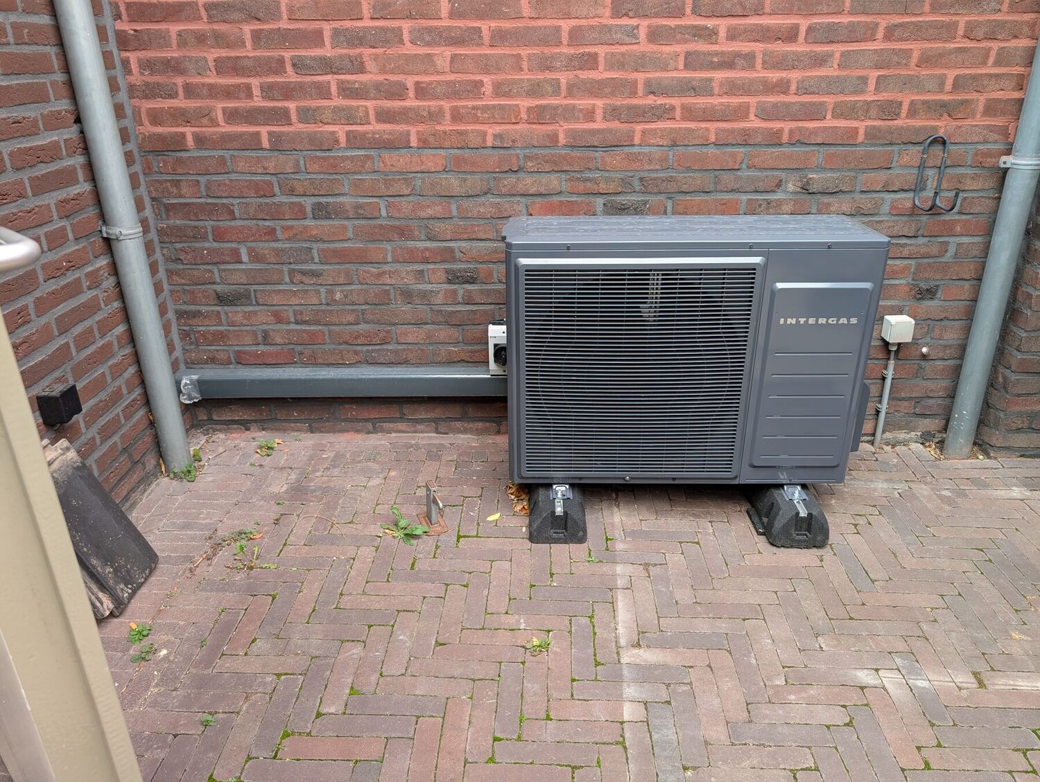 Intergas warmtepomp-buitenunit op trillingsdempers, geplaatst op klinkers tegen de gevel