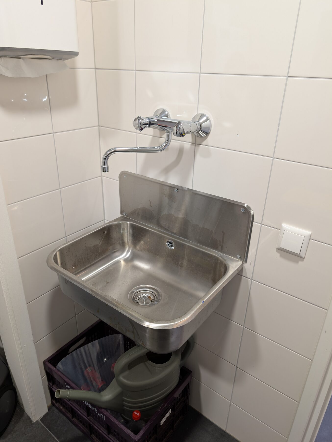 Rvs uitstortgootsteen met wandkraan, aangesloten tegen een betegelde wand