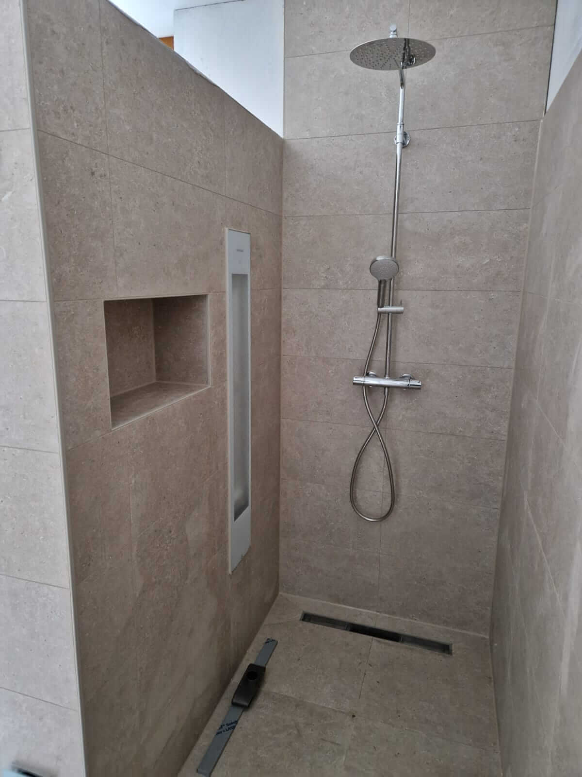Betegelde inloopdouche met regendouche, nis en douchegoot in een badkamer